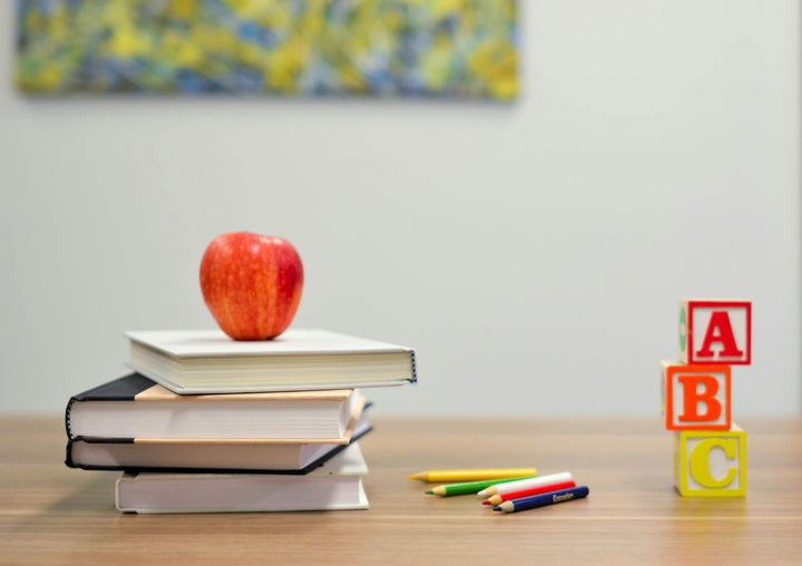 family board game for home school over stack of books with an apple on top, surrounded by colorful pencils and ABC blocks on a wooden surface