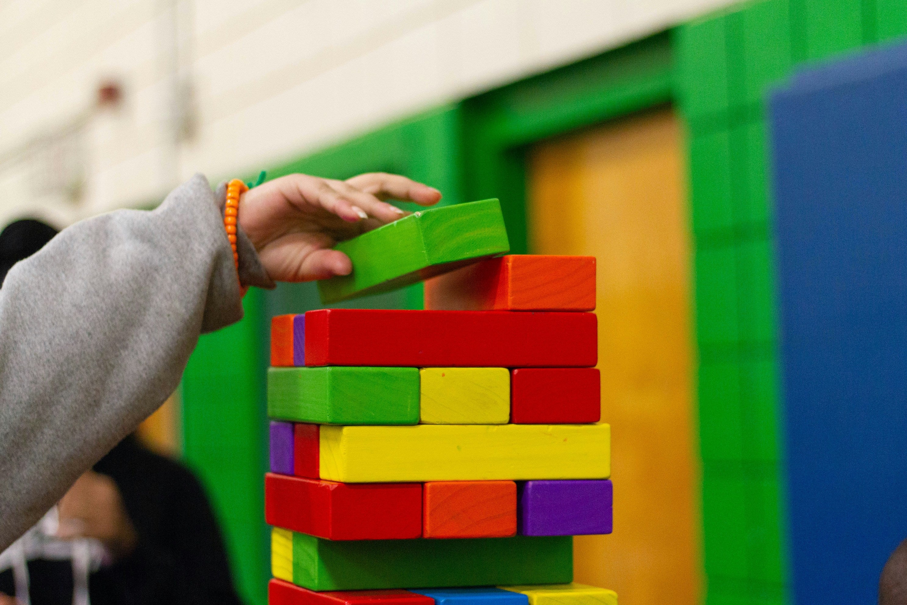 candygrams word game “play is our favorite way of learning” over colorful building blocks being stacked by a child's hand 